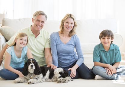 Auto Plus Insurance Group LLC | A family sitting on their living room floor in front of a couch smiling with their dog